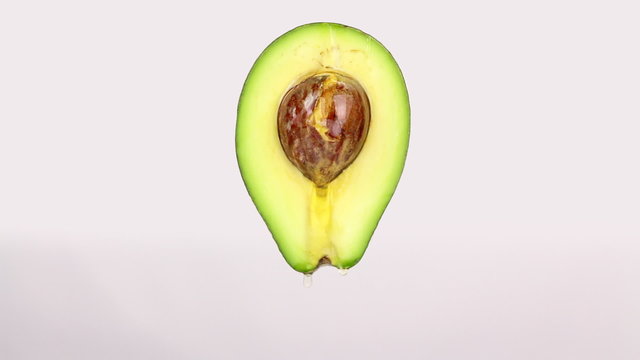 Oil drops from a half cut avocado on a white background