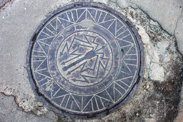 Manhole with metal cover in the cracked asphalt surface