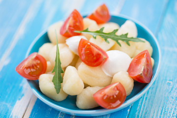 Boiled italian gnocchi with sliced cheese, tomatoes and arugula