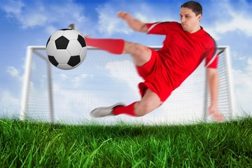 Fit football player jumping and kicking ball