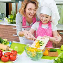 Smiling mother and daughter cooking a salad.