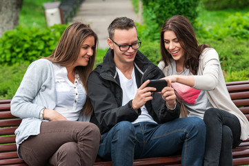 Group of friends sitting on a bench in the park and enjoying