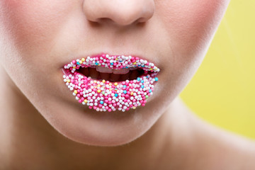 Beautiful woman's mouth full of colorful sugar pearls