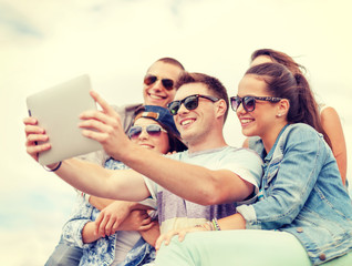 group of smiling teenagers looking at tablet pc