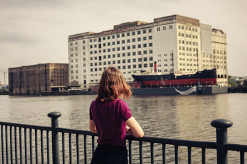 Fototapeta na wymiar Young woman relaxing by river and looking across at buildings
