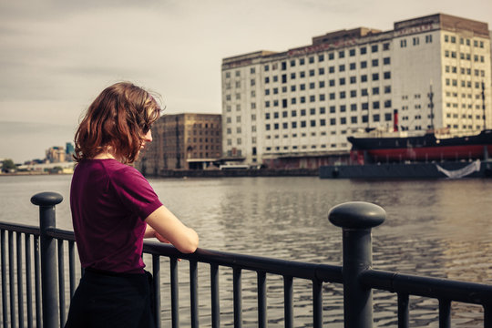 Young woman relaxing by river and looking across at buildings