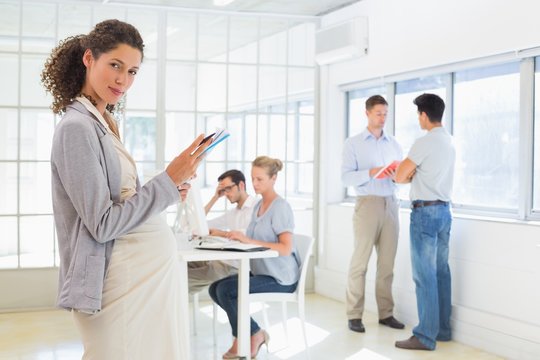 Pregnant businesswoman looking at camera with team behind her