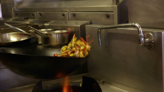 Chef tossing vegetables in a wok over a large flame