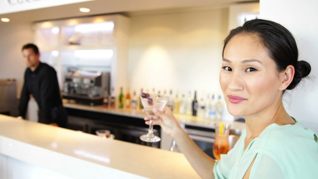 Asian woman smiling at camera drinking a cocktail