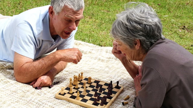 Senior couple relaxing in the park lying on a blanket playing ch