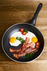 Scrambled eggs and bacon on frying pan on table close-up