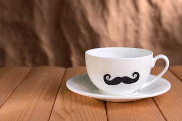 Cup with mustache on table on brown background