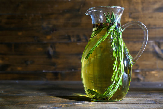 Essential Oil with rosemary in glass jug, on wooden background
