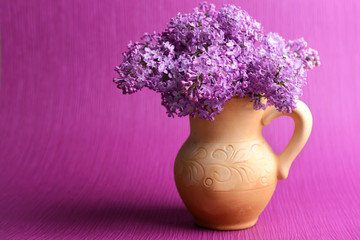 Beautiful lilac flowers in pitcher on purple background