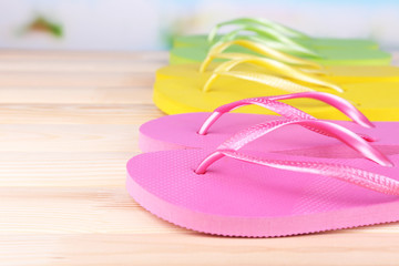 Bright flip-flops on wooden table, on nature background