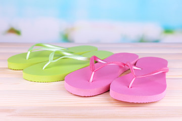 Bright flip-flops on wooden table, on nature background