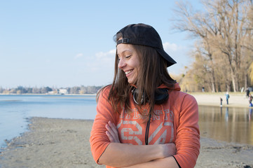 Girl smiling and listening music in baseball cap at the lake