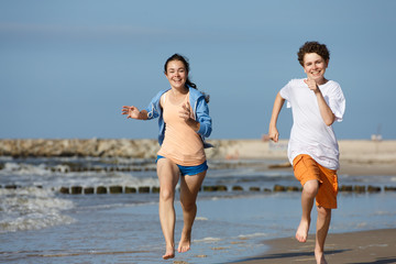 Teenage girl and boy running, jumping on beach