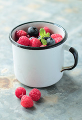 Old tin mug with blueberry and raspberry fruits