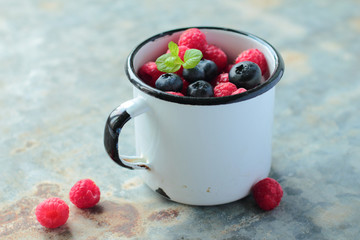 Tin enamel mug full of blueberry and raspberry fruits