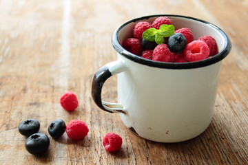 Tin mug with fresh fruits of raspberries and blueberries