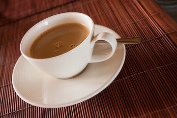 Steaming hot cup of black coffee on wooden tablemat