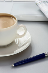 cup of coffee near the laptop and newspapers