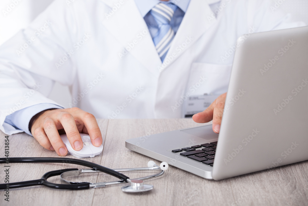Poster midsection of doctor using laptop and mouse at desk