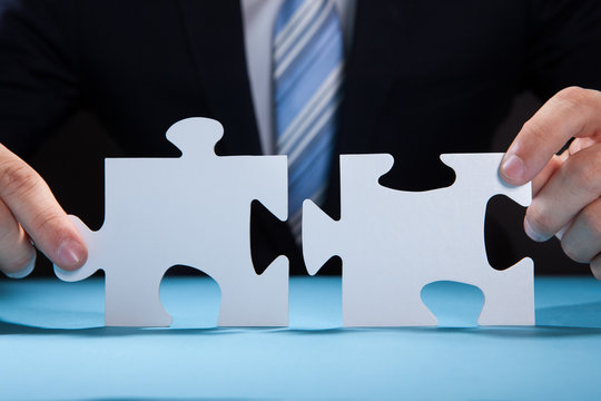 Businessman Joining Puzzle Pieces At Desk
