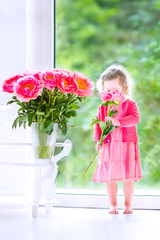 Pretty toddler girl playing with peony flowers