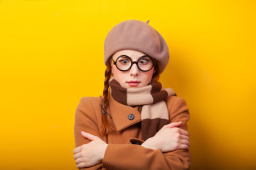 Redhead girl in coat and scarf on yellow background.