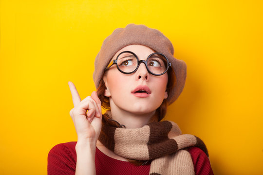 Redhead girl in glasses and scarf on yellow background.