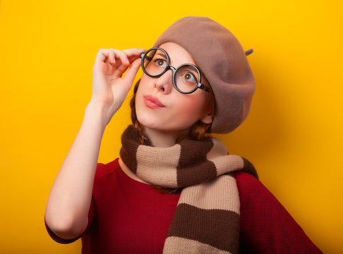 Redhead girl in glasses and scarf on yellow background.