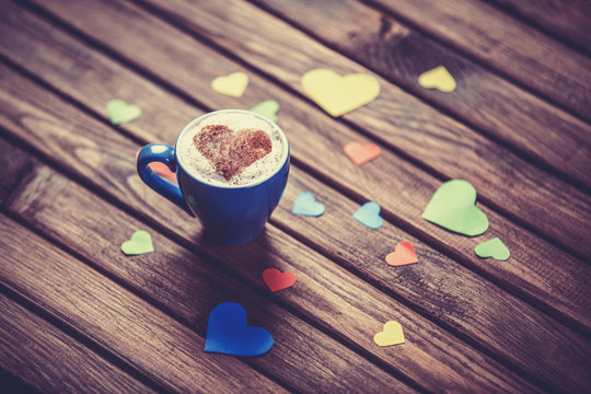 Cup with coffee and heart shape papers on wooden table.