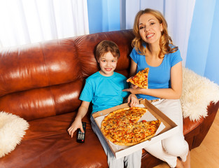 Happy boy and mother eating pizza on the couch