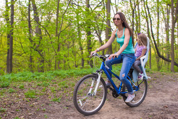 Happy mother and little daughter cycling bicycle at the park