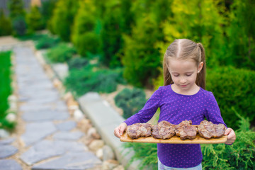 Adorable little girl with grilled steaks in the hands outdoor