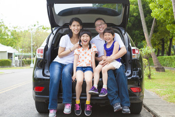 happy family sitting in the car and their house behind