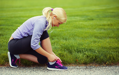 Woman runner tying running shoes. Blonde Girl over Green Grass