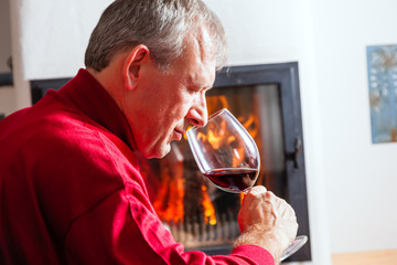 Mann trinkt Rotwein am Kamin