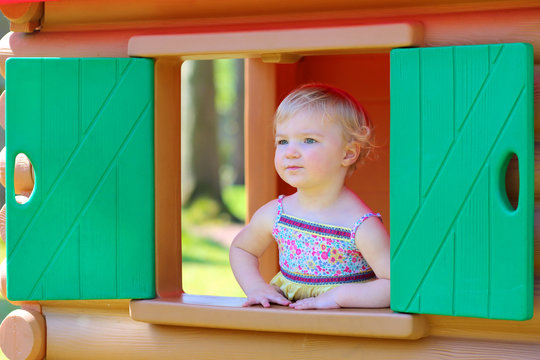 Little Girl Having Fun Outdoors Hiding In Plastic Playhouse