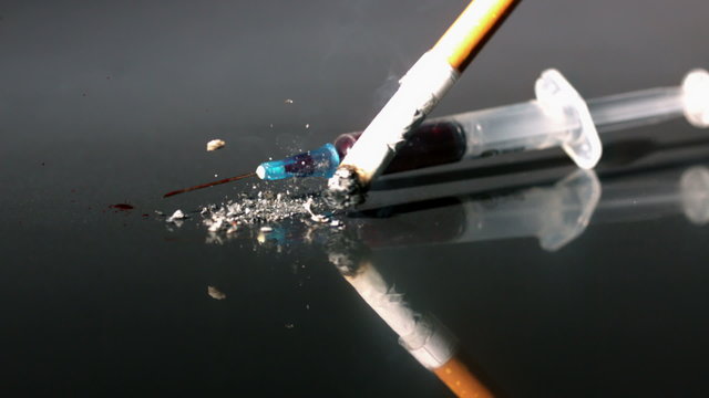 Cigarette and syringe falling onto reflective surface