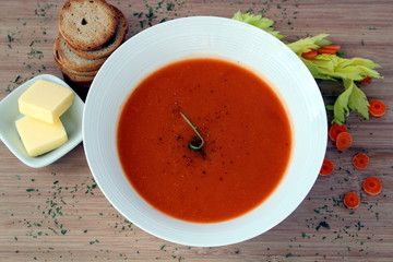 Carrot soup in a white bowl, with crackers and butter