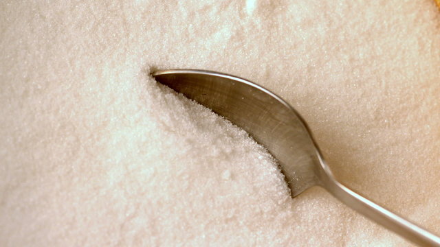 Teaspoon scooping up white sugar