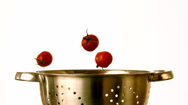 Cherry tomatoes falling into colander on white background