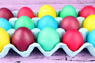 Colorful Easter eggs in tray on wooden background