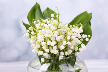 Beautiful lilies of the valley in glass vase on light