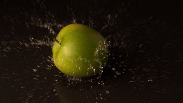 Green apple falling on wet black surface