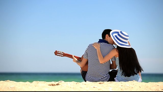 Young couple with guitar on the beach in summer day.