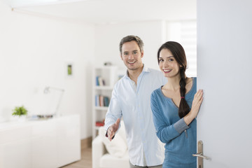 Cheerful couple inviting people to enter in home